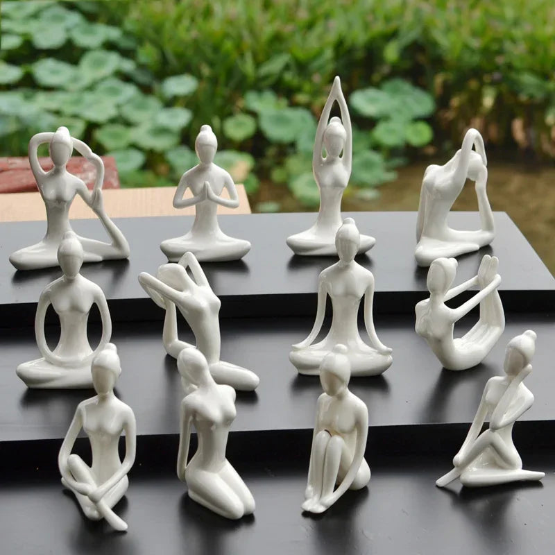 Set of white ceramic yoga pose statues arranged on black platforms with green garden background