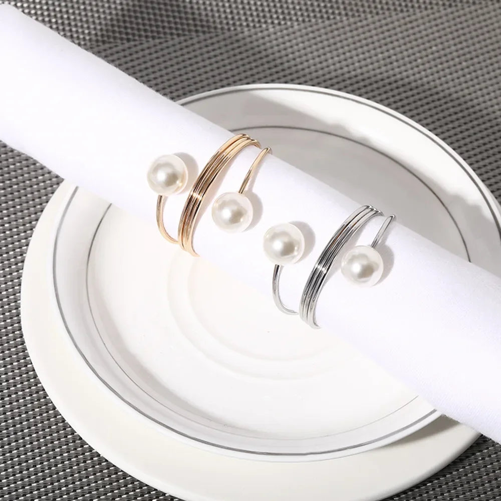 Elegant gold and silver napkin rings with pearl accents displayed on white plate with silver trim
