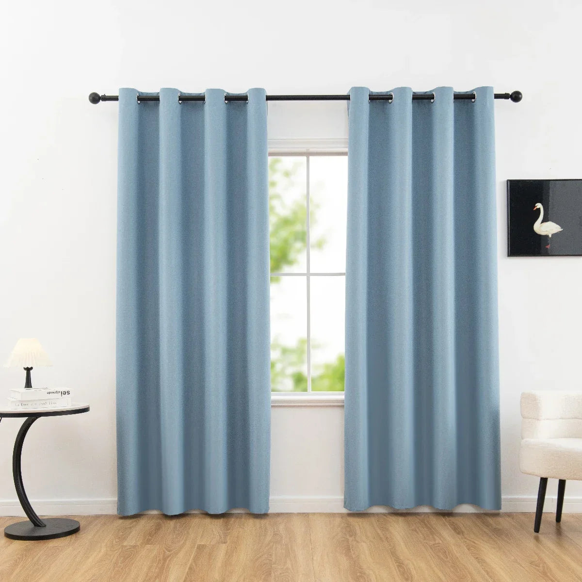 Light blue blackout curtains with metal grommets hanging on black rod in bright living room with wooden floor