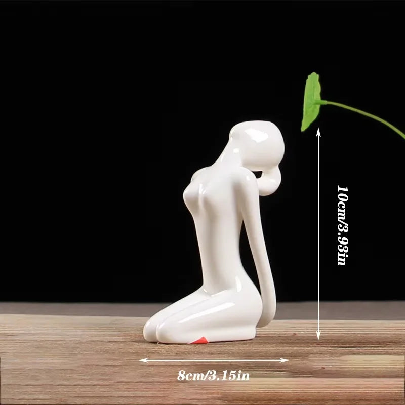 White abstract ceramic sculpture of a kneeling human figure holding a green leaf, 10cm tall, 8cm wide