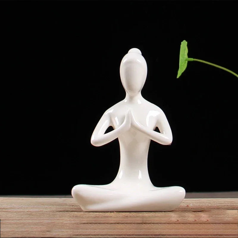 White ceramic figurine of a person in lotus yoga pose with hands in prayer on wooden surface, black background
