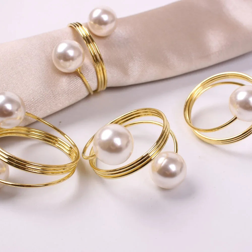 Elegant gold rings with large white pearls displayed on a light beige fabric and white surface
